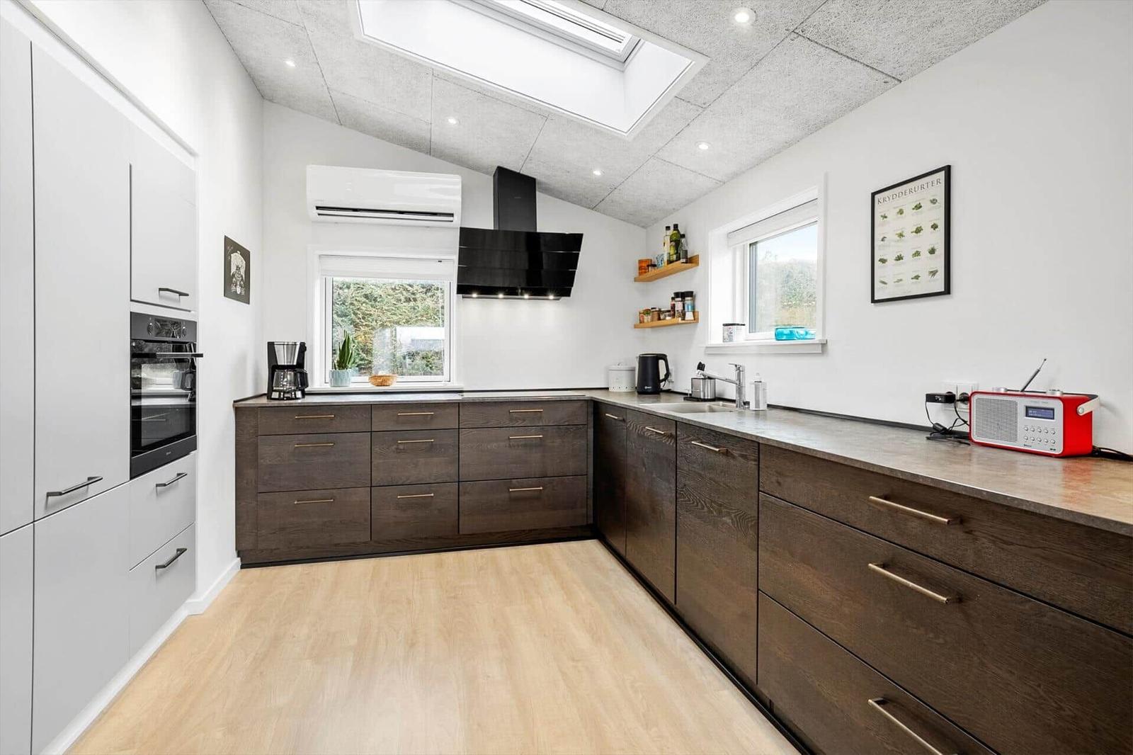 Moderne Küche mit dunklen Schränken, weißen Wänden und Holzboden. Fenster und Dachfenster sorgen für Tageslicht.