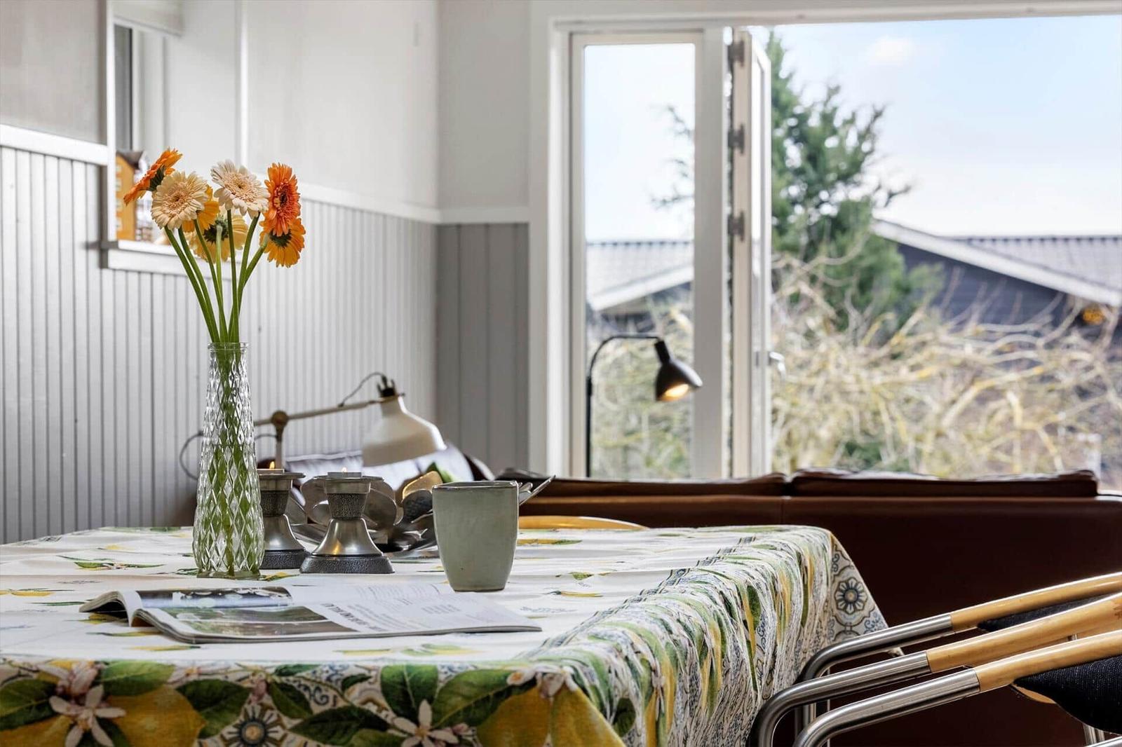 Tisch mit Blumen, Tasse und Zeitschrift vor Fenster mit Blick nach draußen.