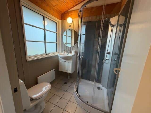 Badezimmer mit Dusche, Waschbecken und Toilette. Holzdecke und Fenster.