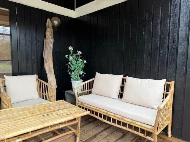 Terrasse mit Bambusmöbeln, Sitzbank und Tisch. Schwarze Holzwand und Pflanze im Hintergrund.