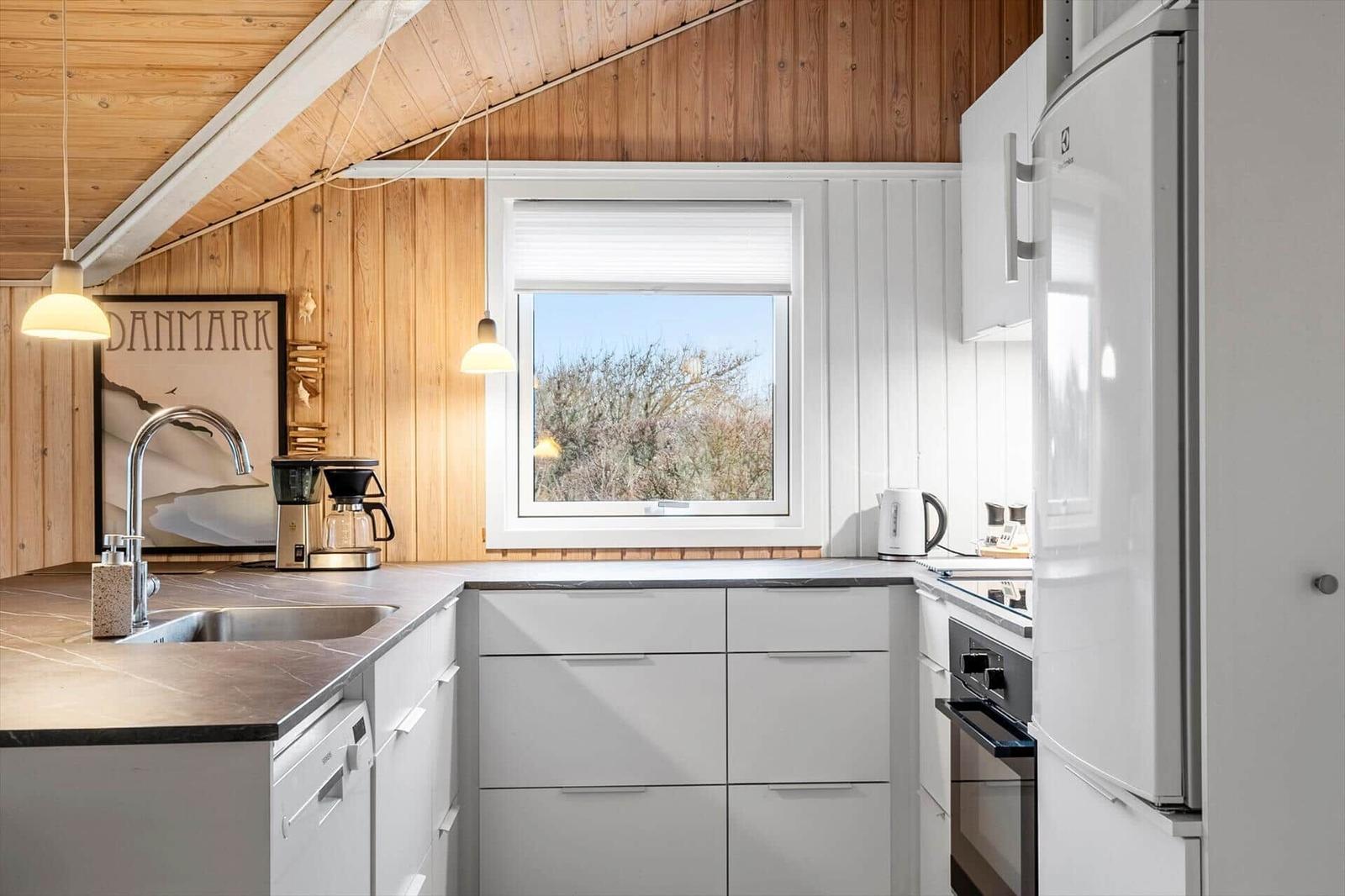 Kitchen with wooden wall, window, and white cabinets.