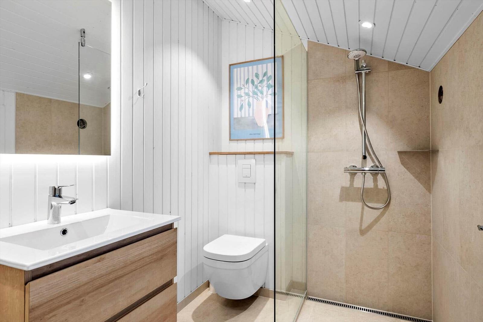 Bathroom with shower, sink, and toilet. Wall cladding and floor tiles.