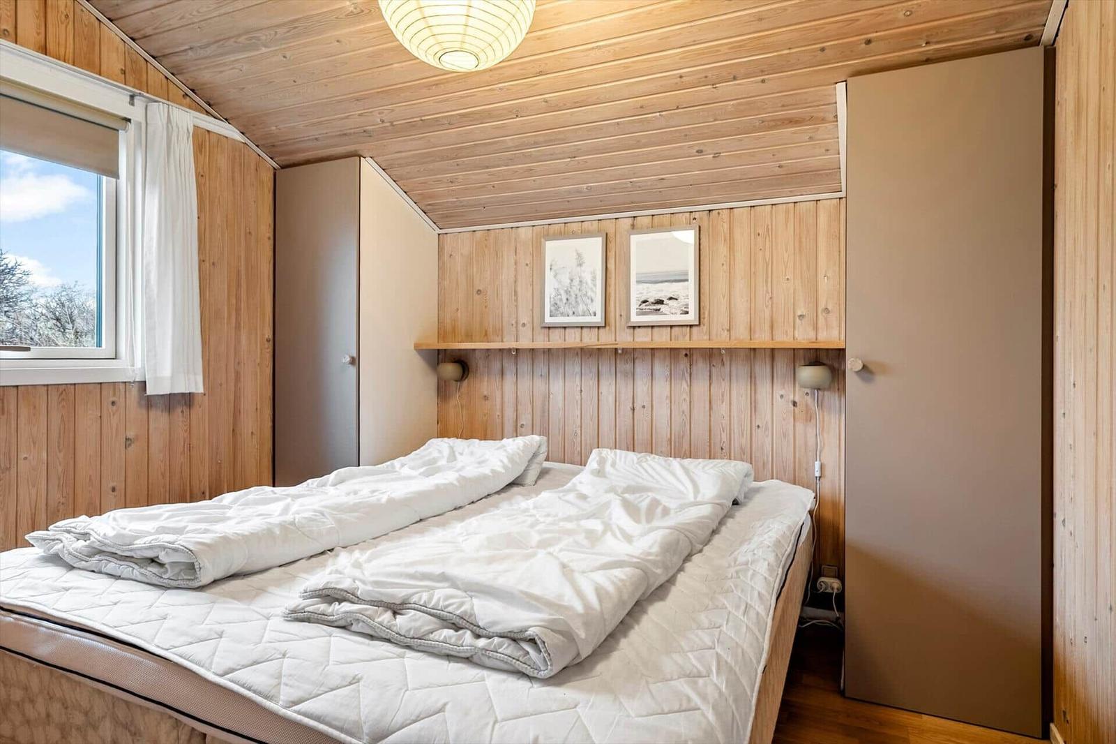 Bedroom with wooden walls, bed, and window. Wall art and ceiling light.