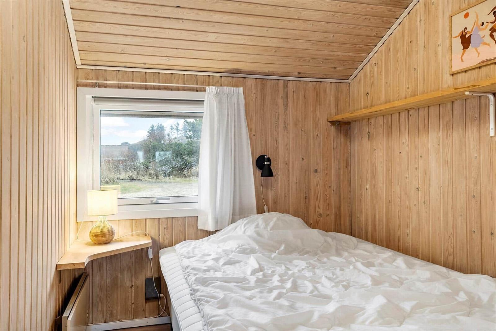Bedroom with wooden walls, bed, window, and nightstand.