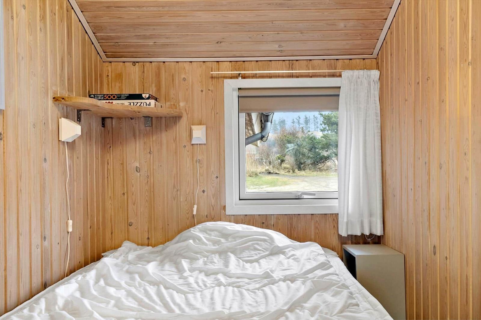 Bedroom with wooden walls, bed, and window overlooking green areas.