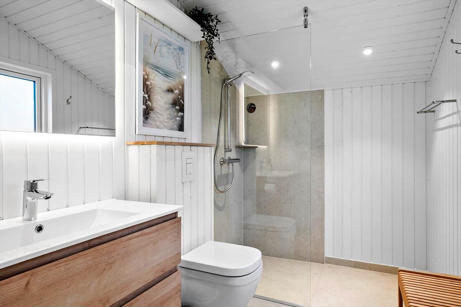 Bathroom with shower, sink, and toilet. White walls and wood accents.