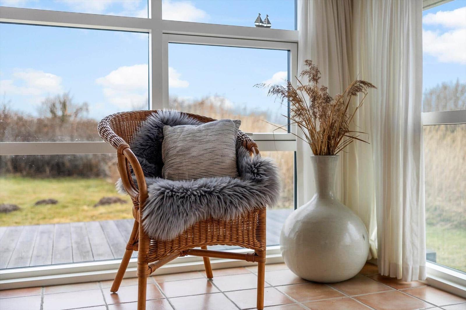 Wicker chair with fur and cushion by large window overlooking green area.