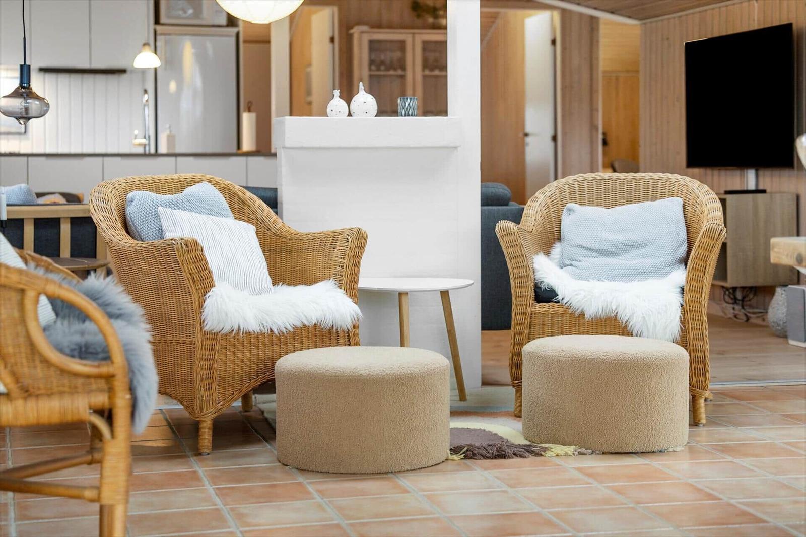 Two wicker chairs with cushions and fur throws stand on terracotta floor.