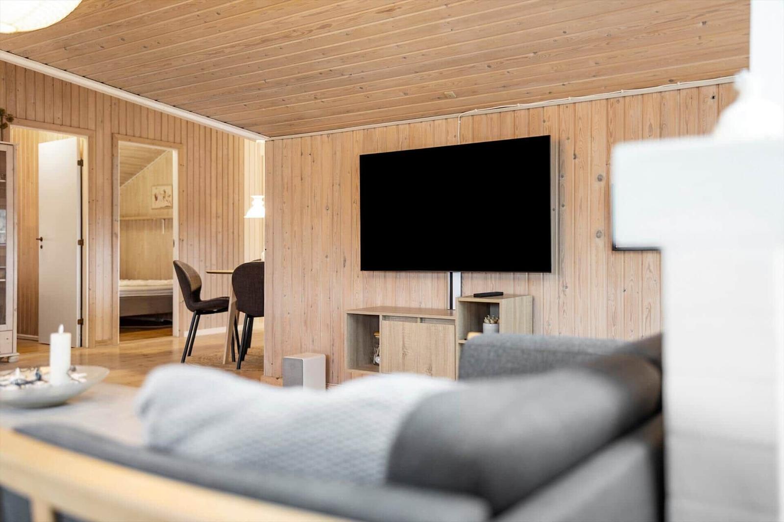 Living room with TV and wooden walls. Dining area visible in the background.