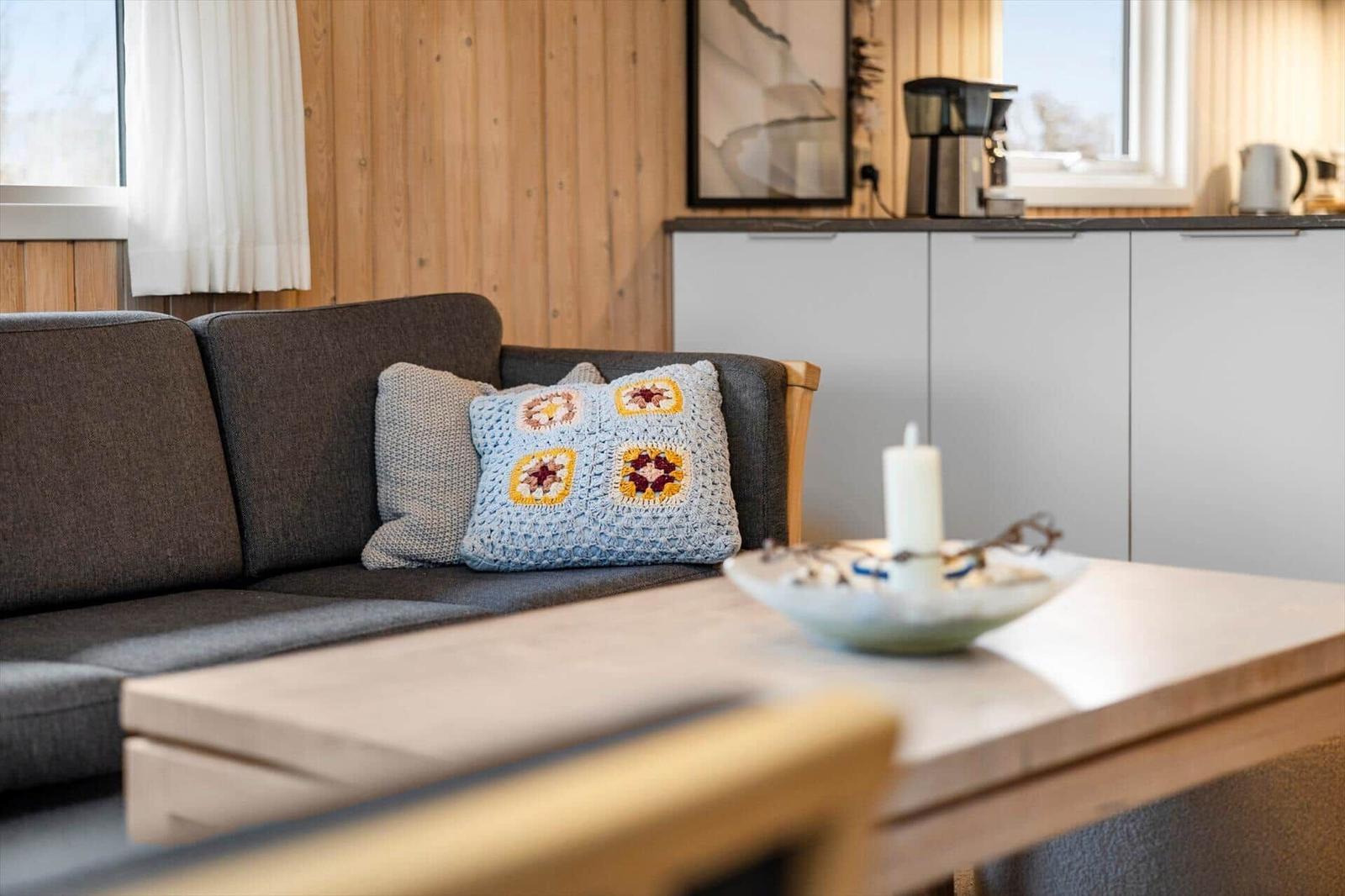A living area with a gray sofa, wooden furniture, and a kitchen counter in the background.