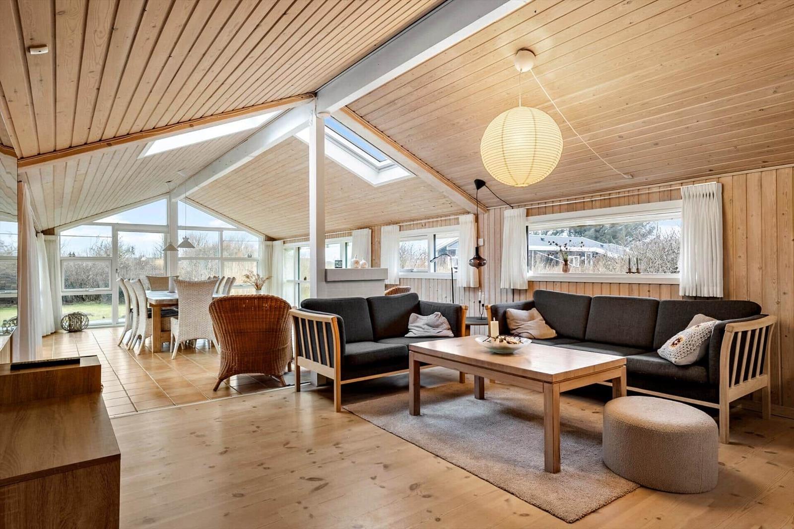 Living and dining area with wooden ceiling, sofa, table, and windows.