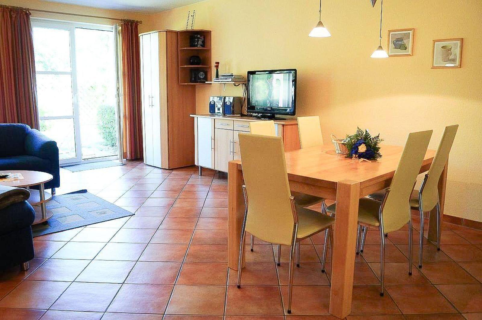 Essbereich mit Holztisch und Stühlen, Fernseher und Schlafzimmer mit Sofa.