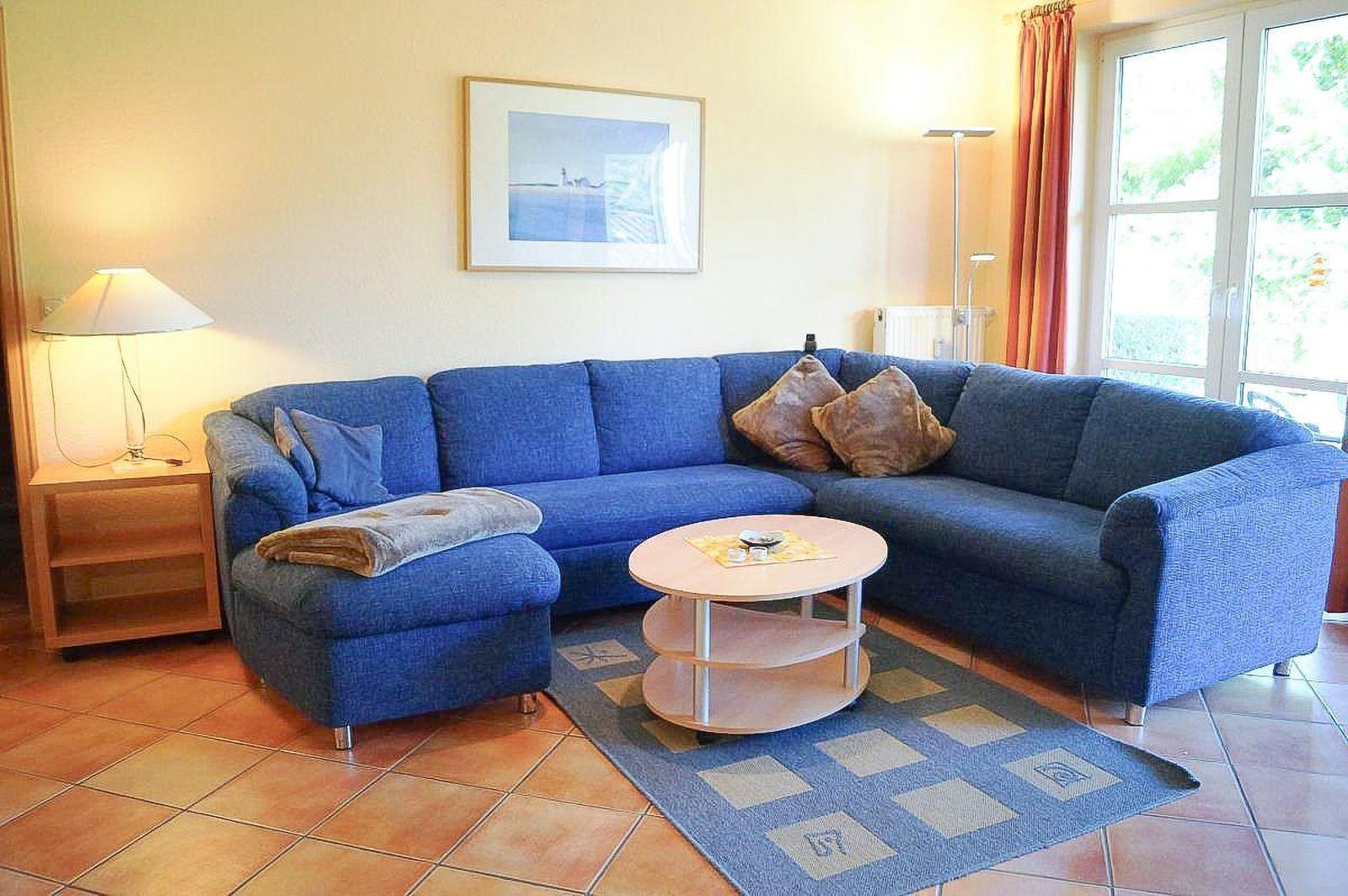 Ein Wohnzimmer mit blauem Sofa, runden Tisch und Teppich.