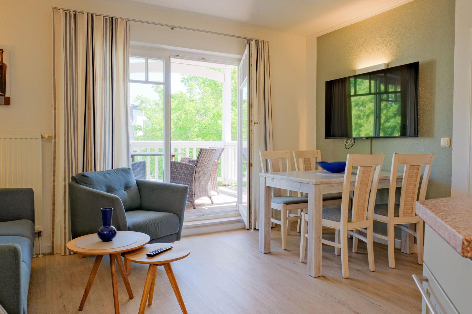 Wohn- und Essbereich mit Balkon, TV und Holzmöbel.