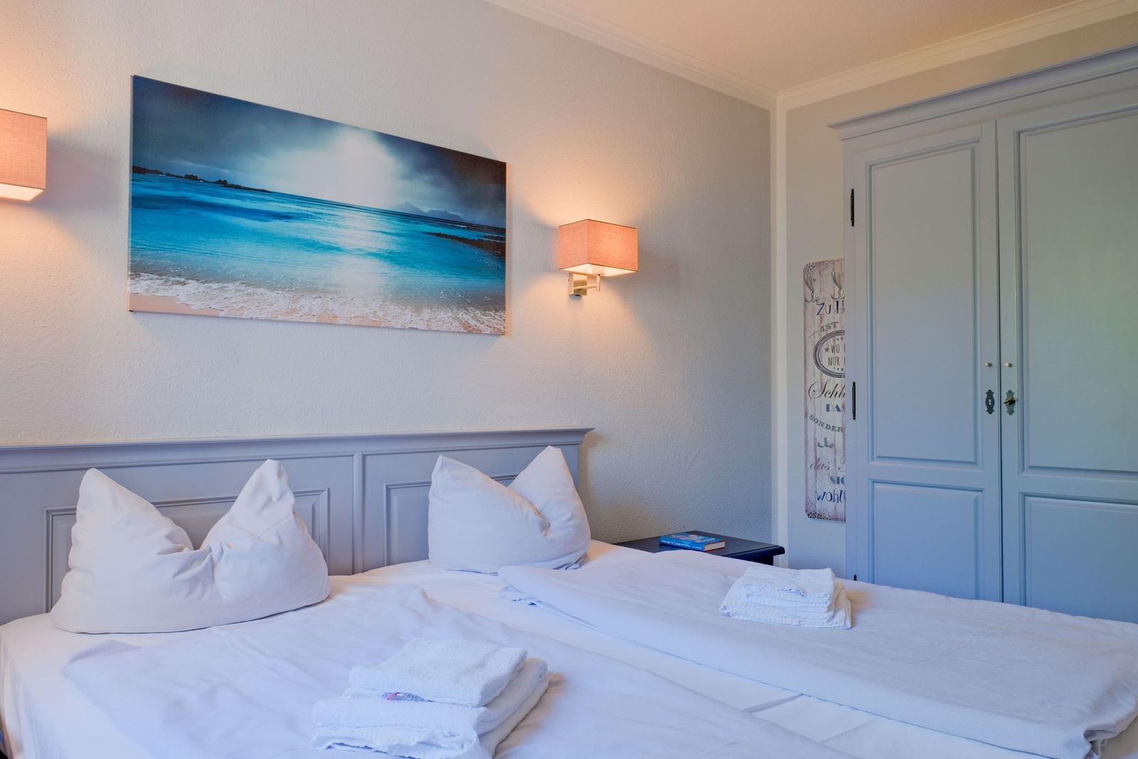 Schlafzimmer mit Doppelbett, Wandbild und Kleiderschrank.