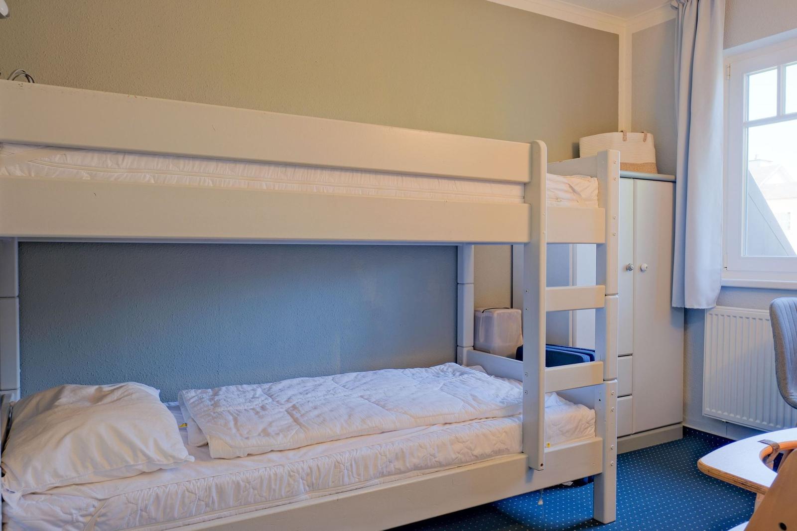 Zimmer mit Doppelstockbett, Kleiderschrank und Fenster.
