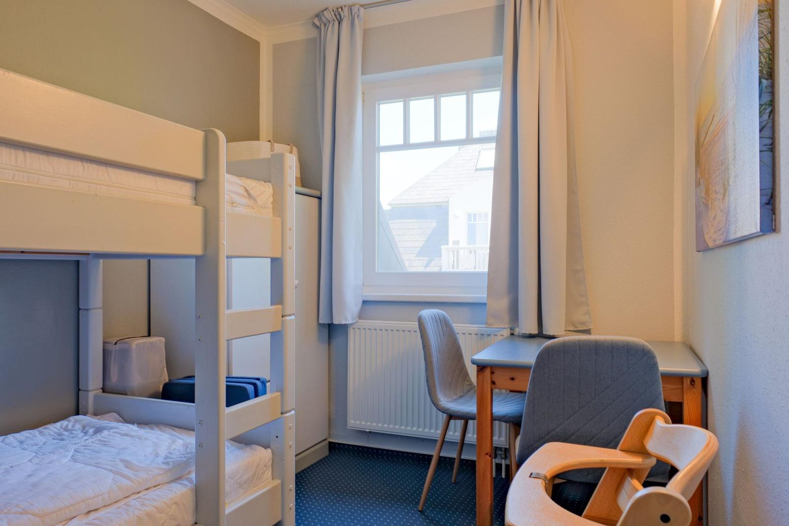 Zimmer mit Doppelstockbett, Schreibtisch und Stühlen. Fenster mit Vorhängen. Wandbild.
