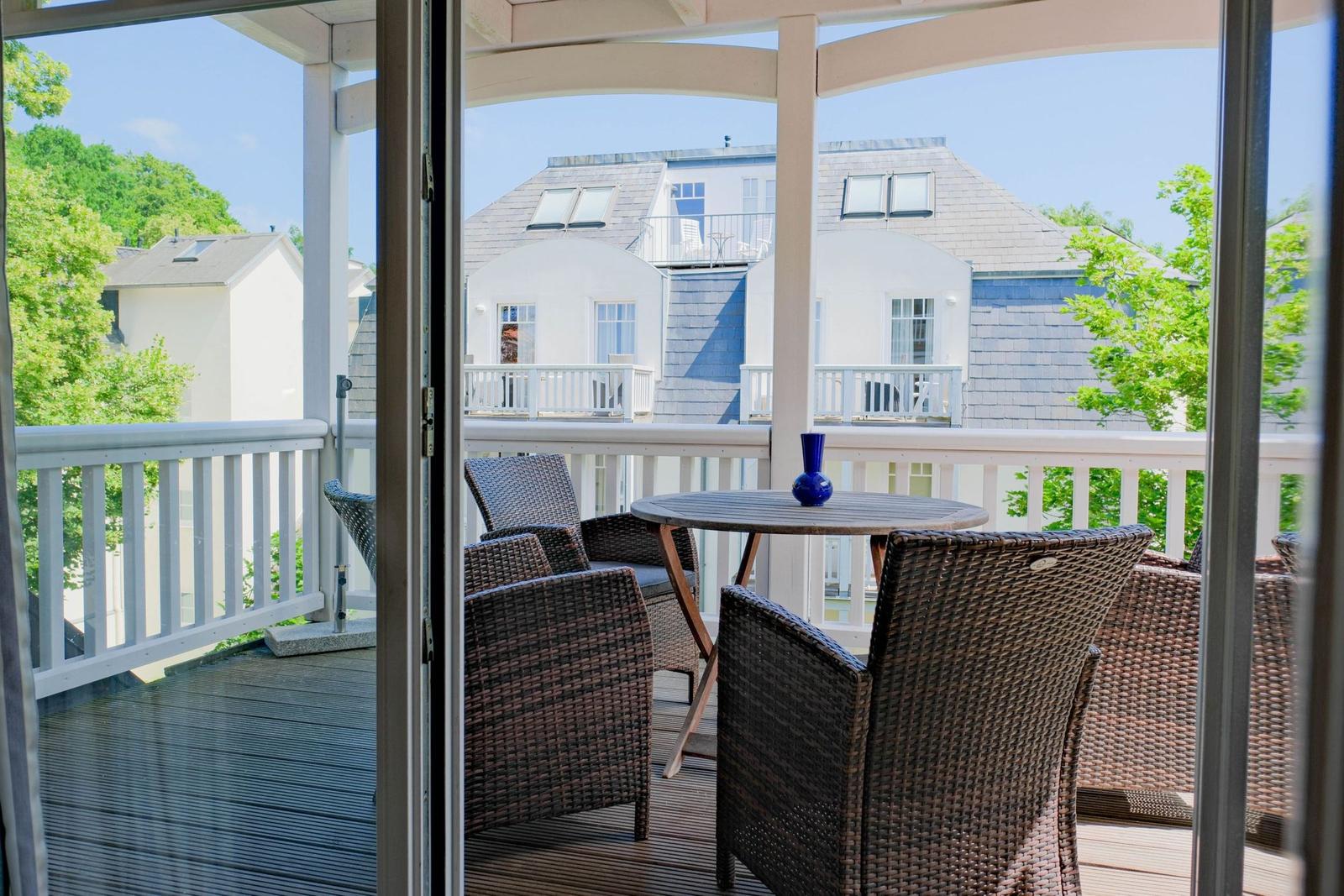 Terrasse mit Tisch und Stühlen, Blick auf weiße Häuser und Bäume.