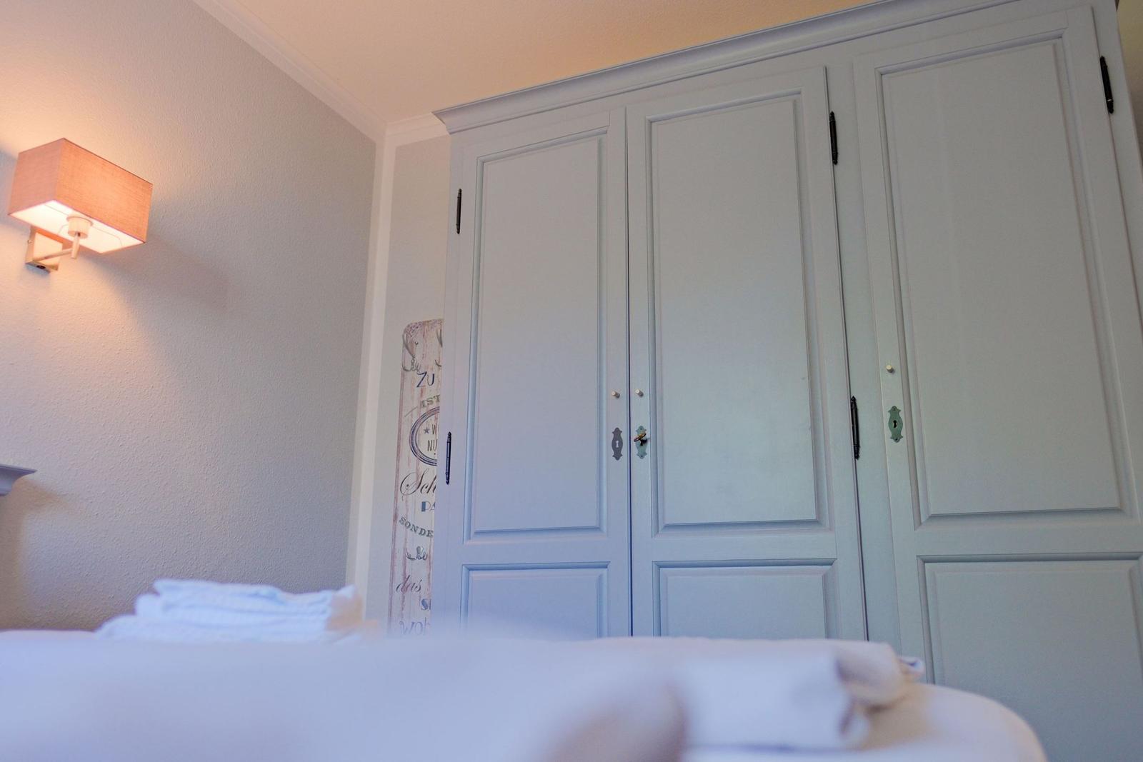 Schlafzimmer mit Bett, Kleiderschrank und Wandlampe.