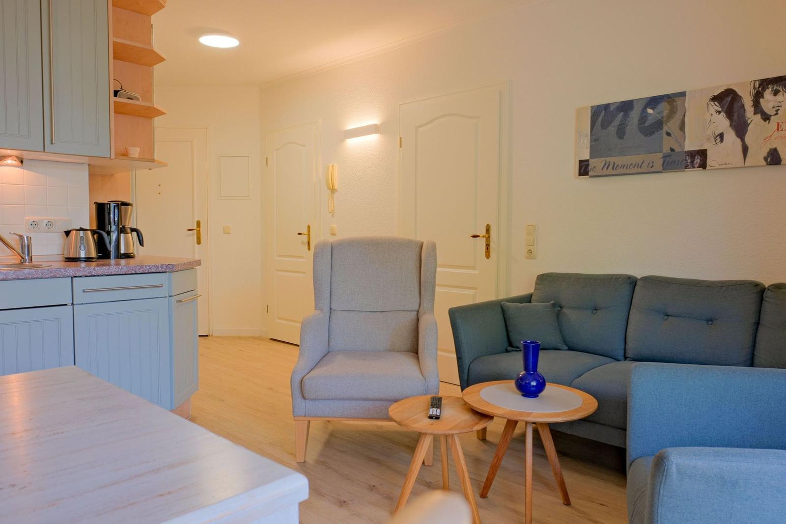 Wohnbereich mit Sofa, Sessel und Küchenzeile. Holzboden und Wandbilder.