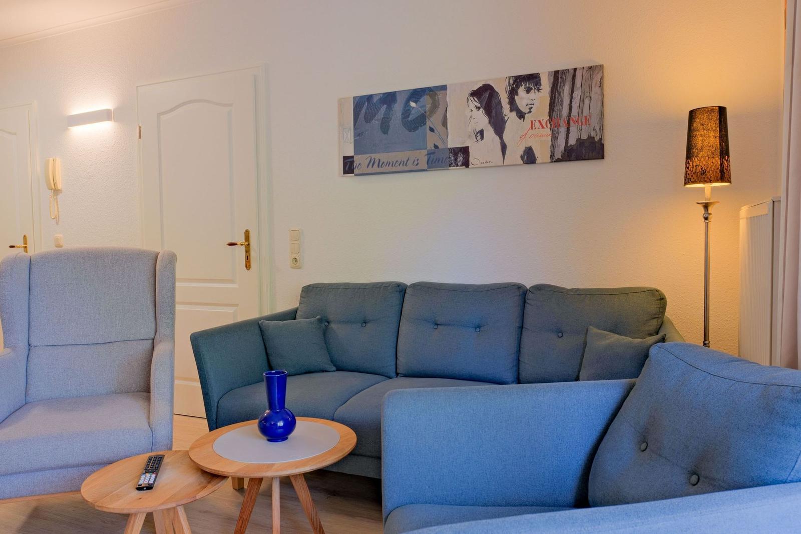 Wohnzimmer mit Sofa, Sessel und Tisch. Wandbild und Stehlampe sichtbar.