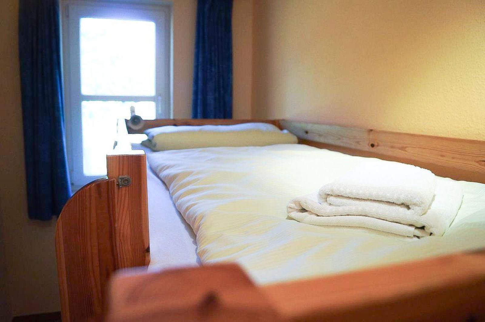 Schlafzimmer mit Holzbett, weißen Bettwäsche und Fenster mit blauen Vorhängen.