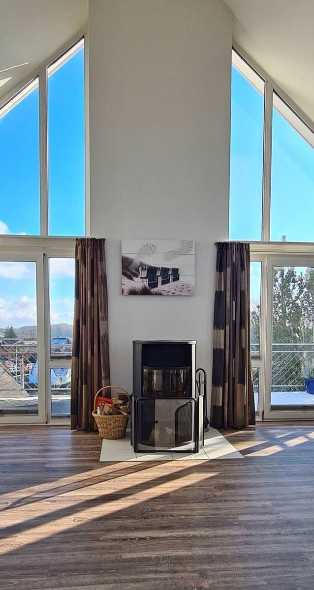 Großes Wohnzimmer mit Kamin und hohen Fenstern. Holzboden und Vorhänge.