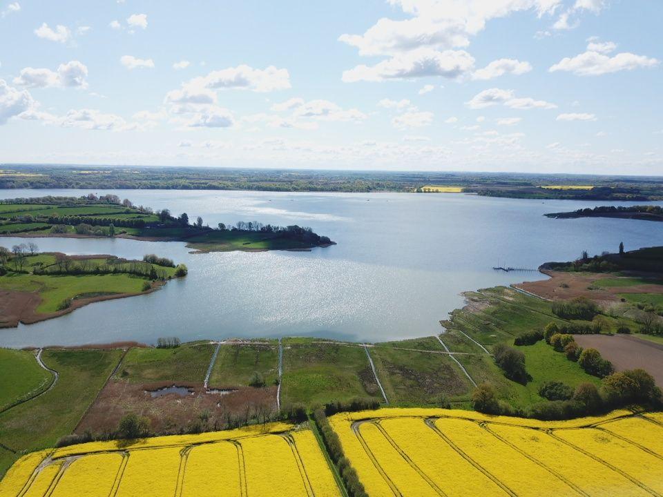 Aerial view of a large lake surrounded by green fields and yellow rapeseed.