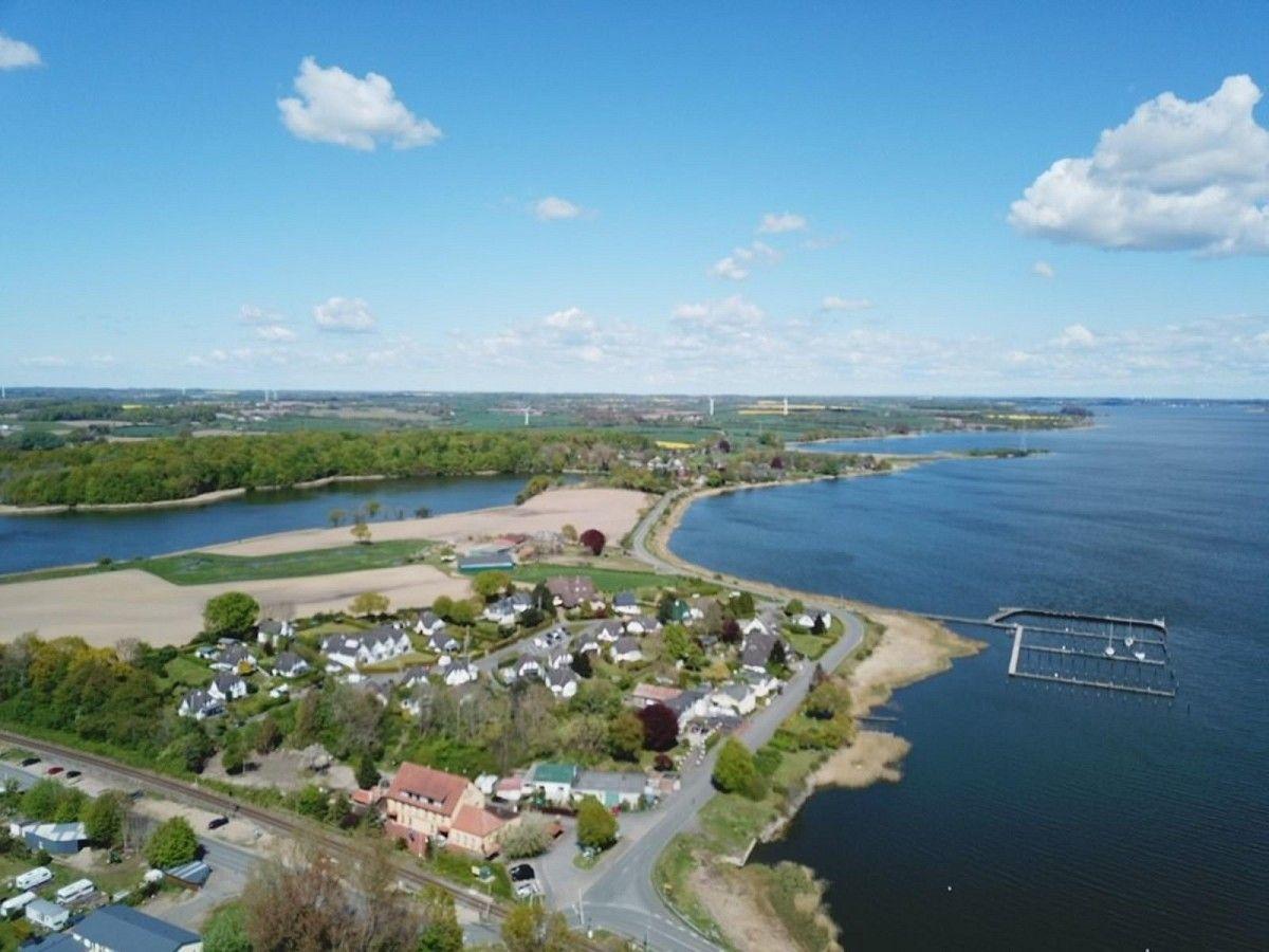 Luftbild einer Küstenlandschaft mit Häusern, Feldern und einem Hafenbecken.