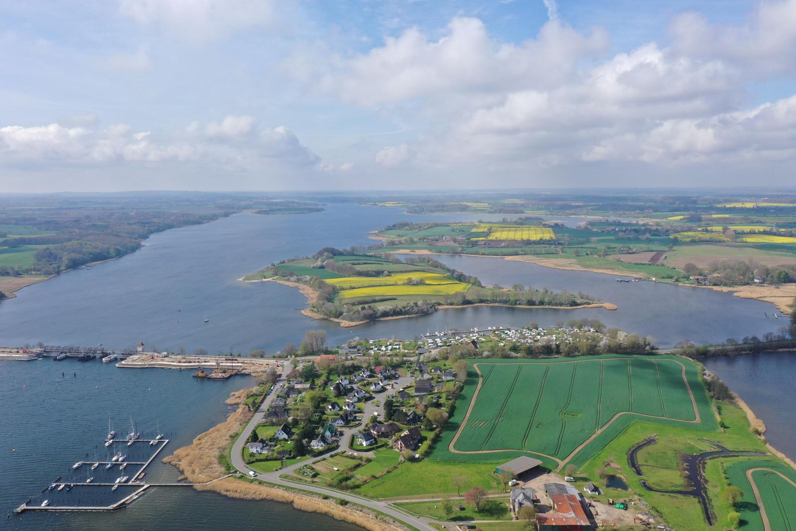 Luftbild einer idyllischen Landschaft mit Fluss, Bootshäfen und grünen Feldern.