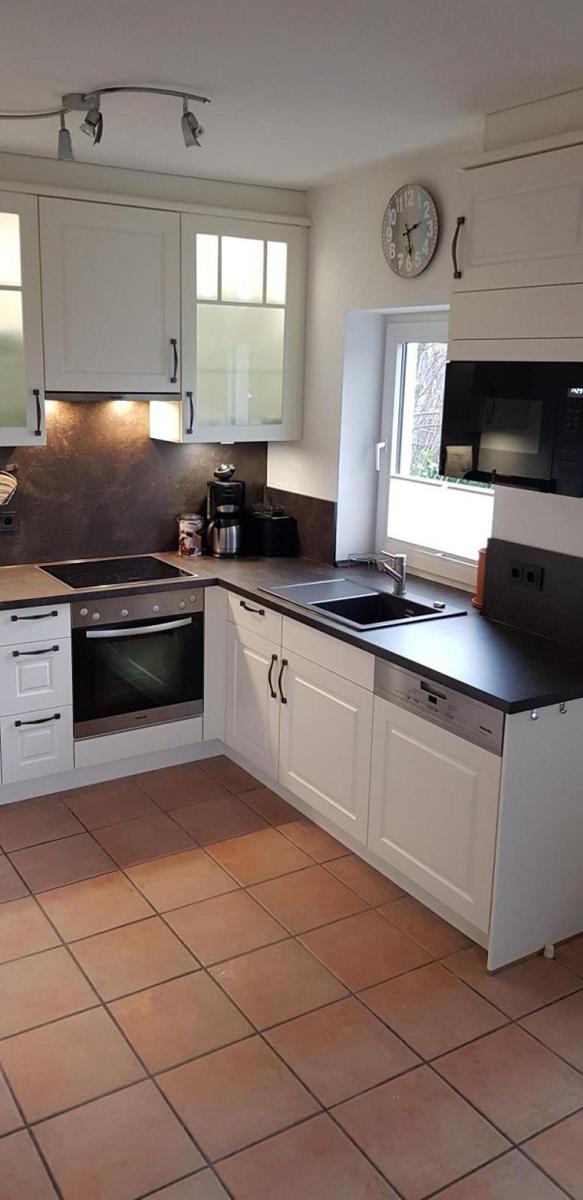 Küche mit weißen Schränken, dunkler Arbeitsplatte und Fenster mit Blick nach draußen.