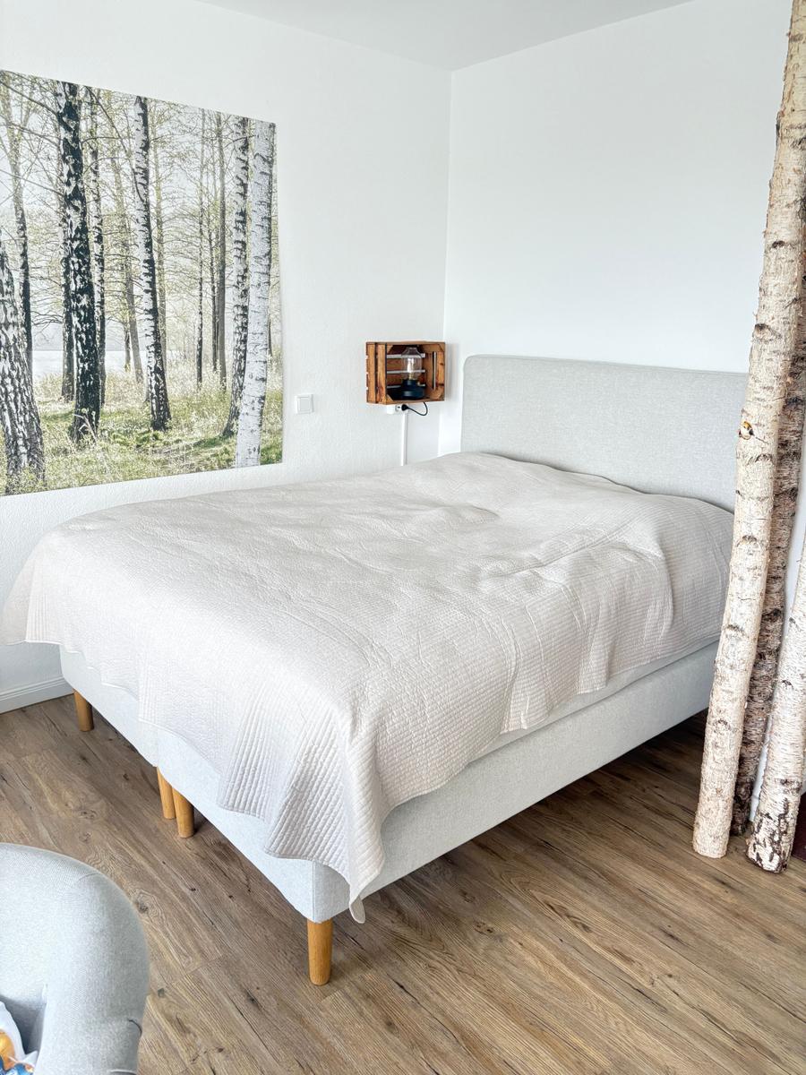 Schlafzimmer mit Bett, Wandbild und Birkenstämmen.