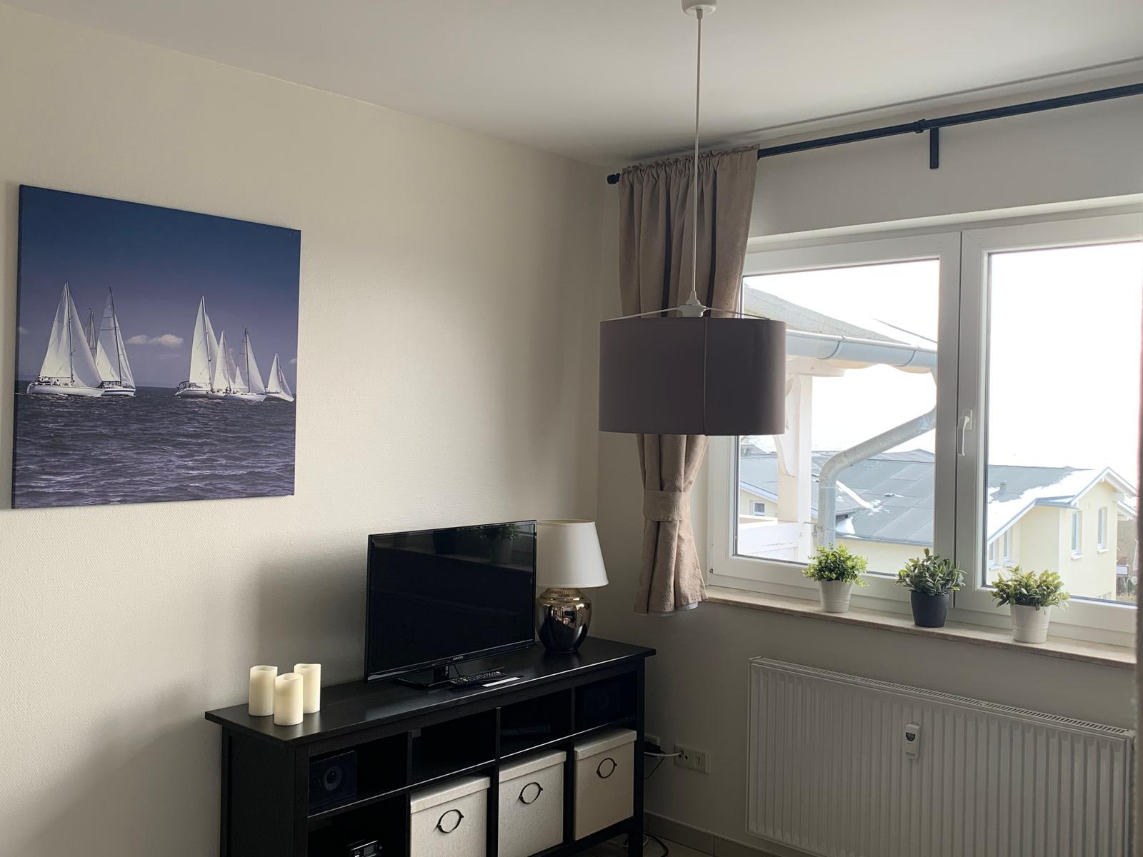 Wohnzimmer mit Fernseher, Wandbild und Fenster mit Pflanzen.