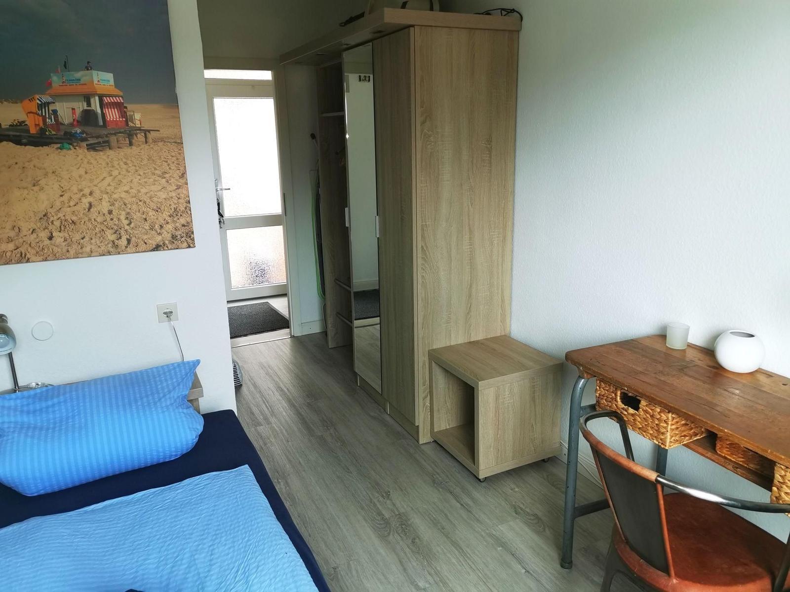 Schlafzimmer mit Bett, Kleiderschrank und Schreibtisch.