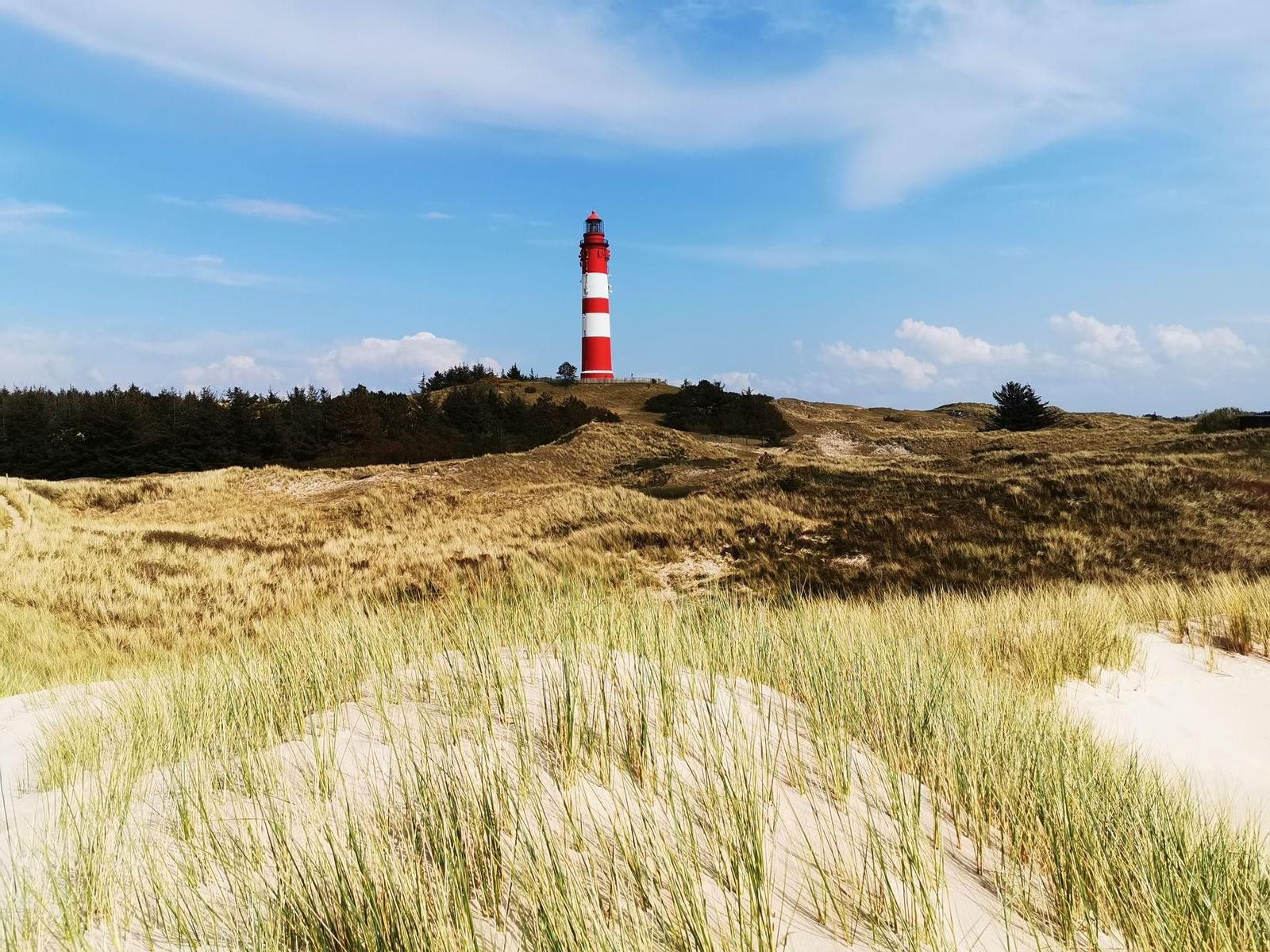 Roter Leuchtturm auf Dünen mit Gras und blauem Himmel.