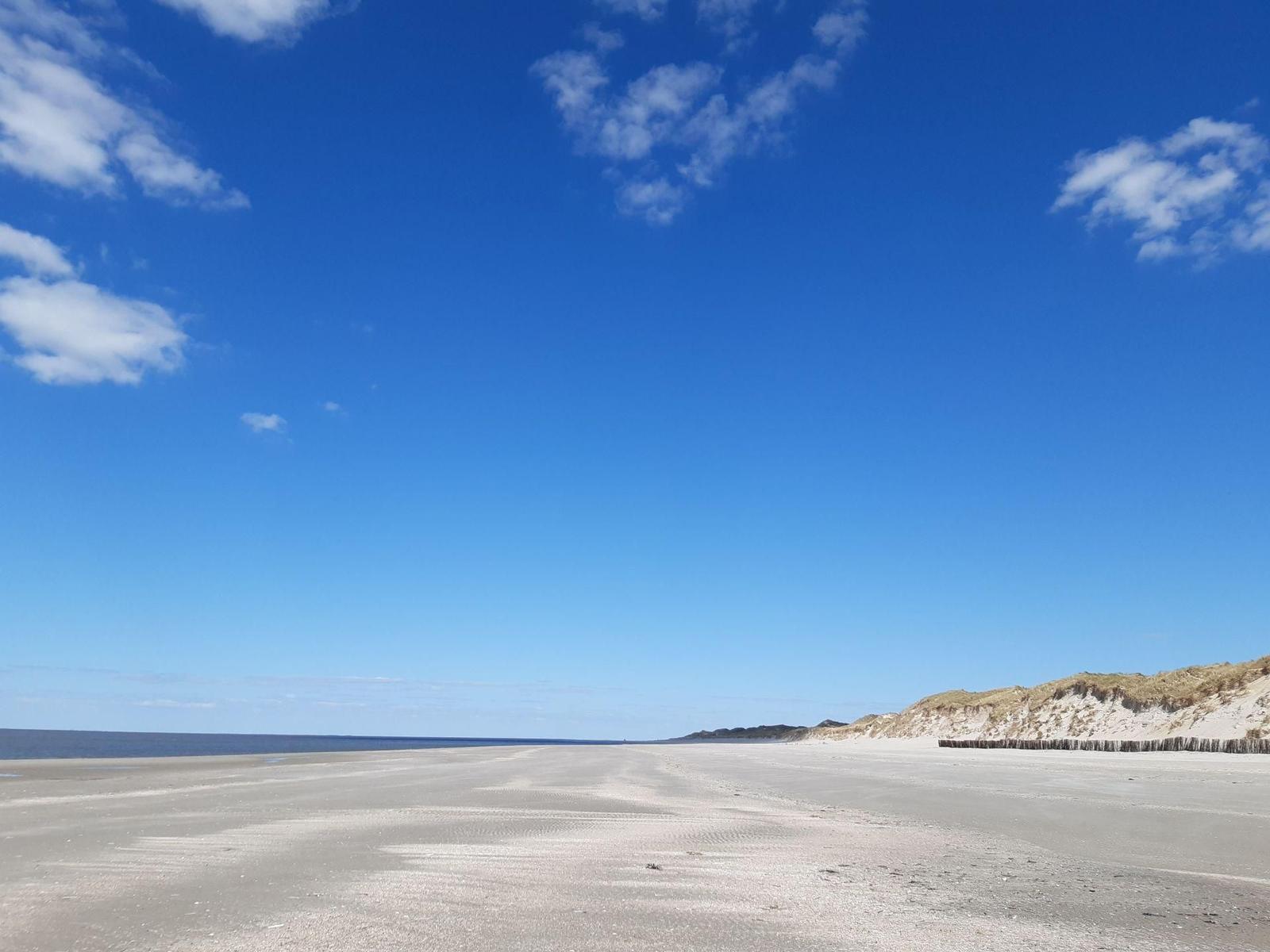 Weiterer Strandabschnitt mit Dünen und blauem Himmel.