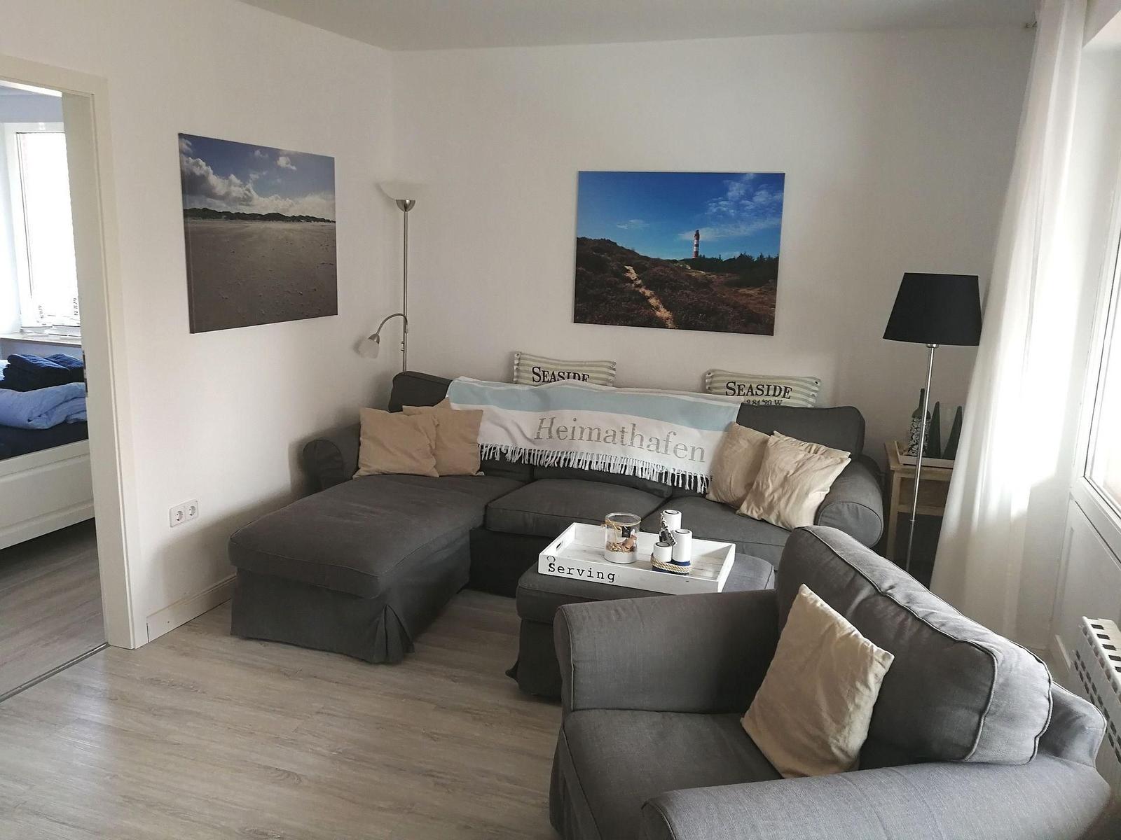 Wohnzimmer mit grauem Sofa, Wandbildern und Holzboden.