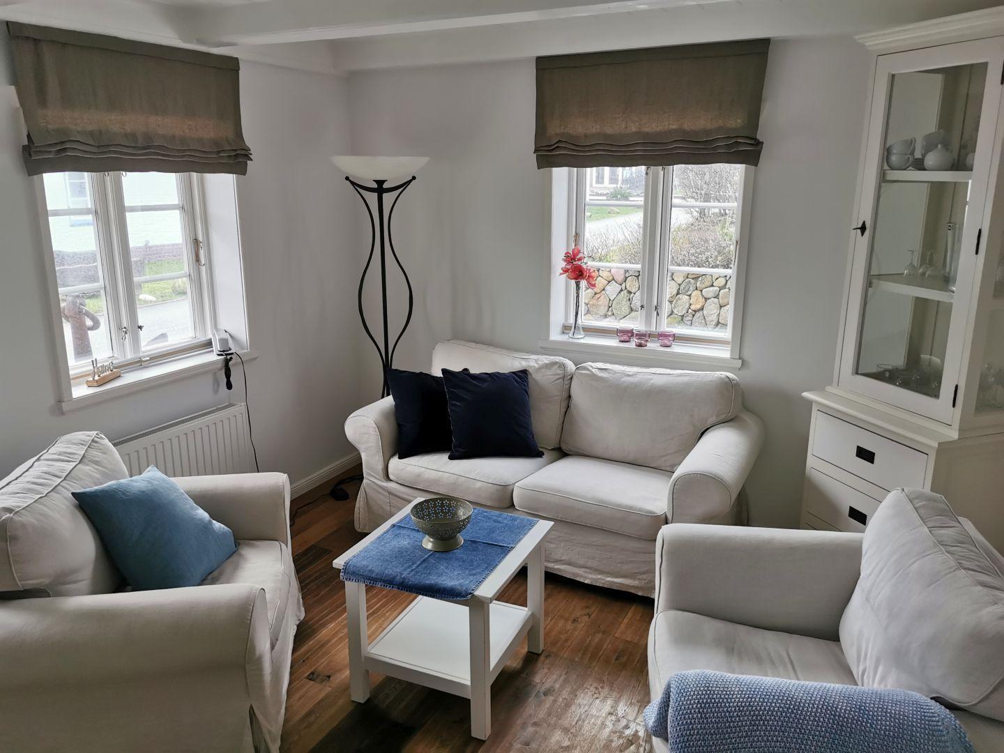 Wohnzimmer mit Sofa, Sesseln und Tisch. Fenster mit Rollladen und Schrank.