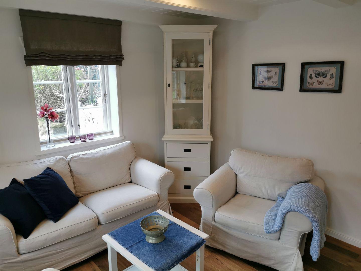 Wohnzimmer mit Sofa, Sessel, Tisch und Glasvitrine.