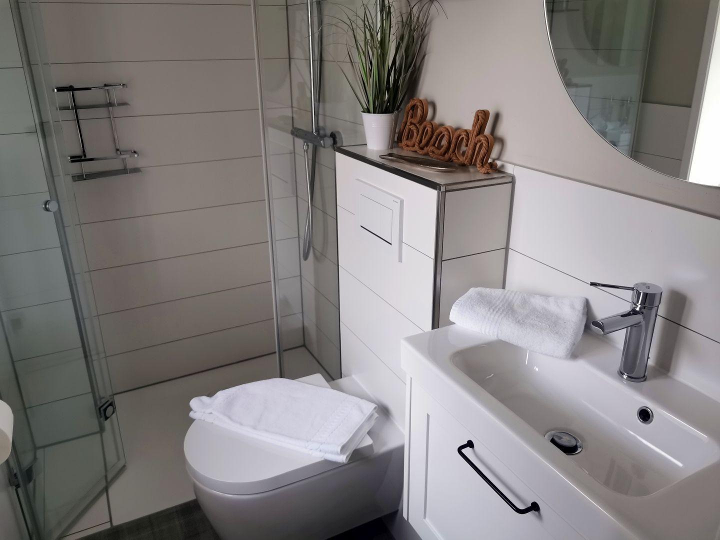 Badezimmer mit Dusche, Toilette und Waschbecken mit Spiegel.