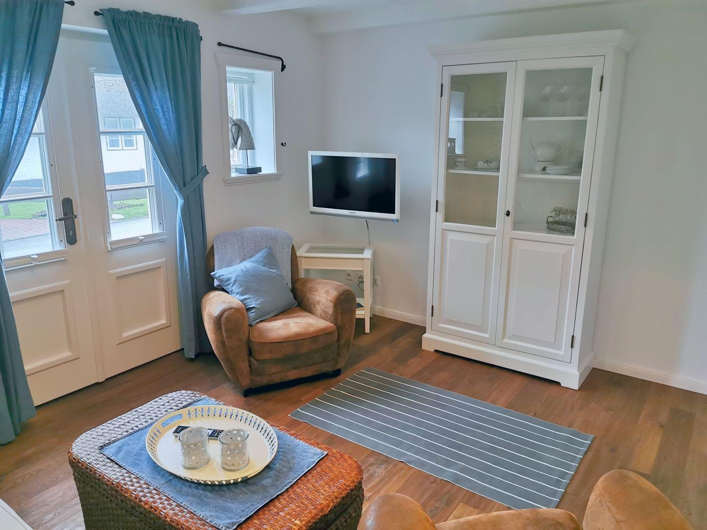 Wohnzimmer mit braunem Sessel, Fernseher und weißen Schränken.