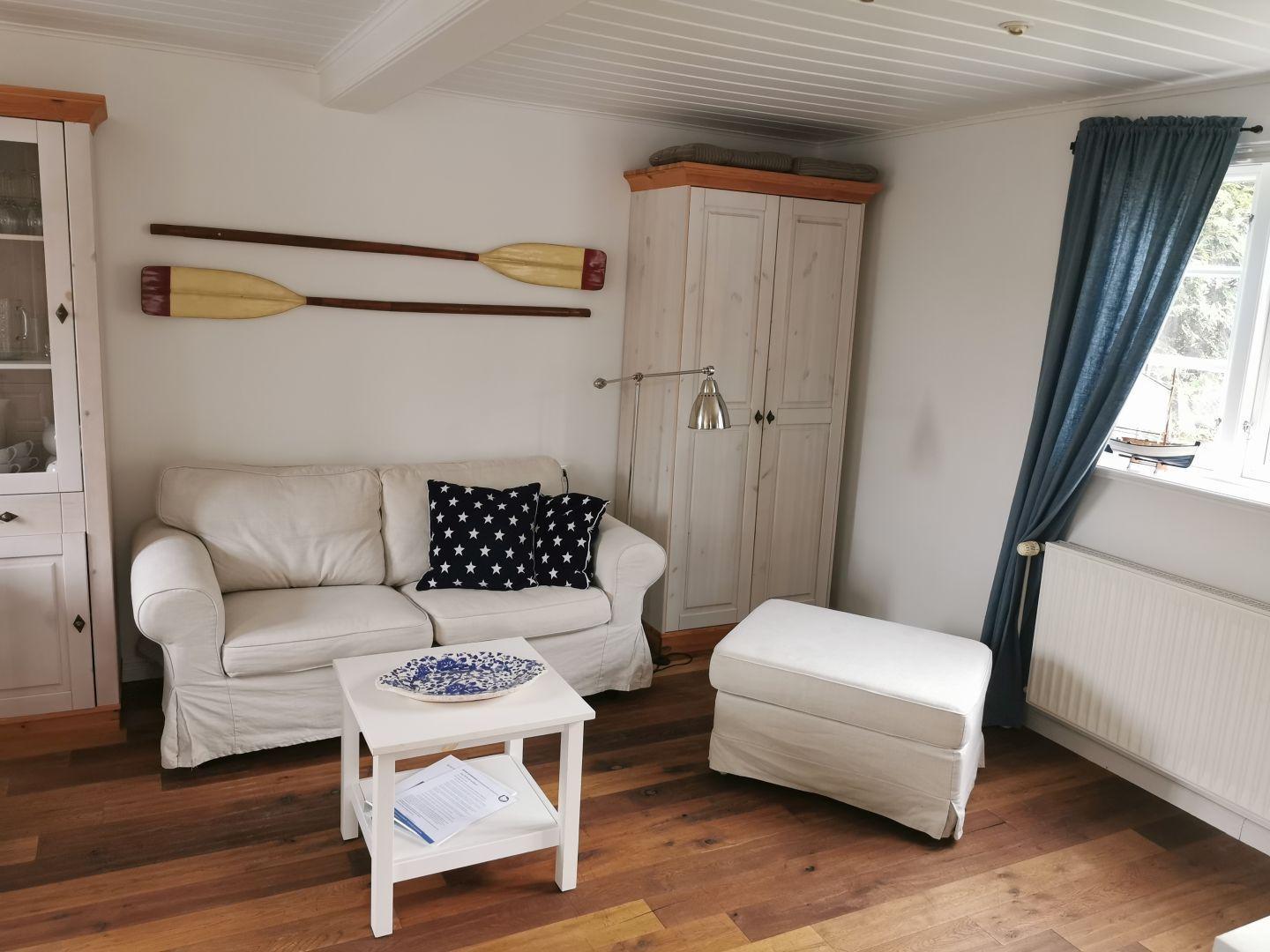Wohnzimmer mit Sofa, Tisch und Schrank. An der Wand hängen zwei Ruder.