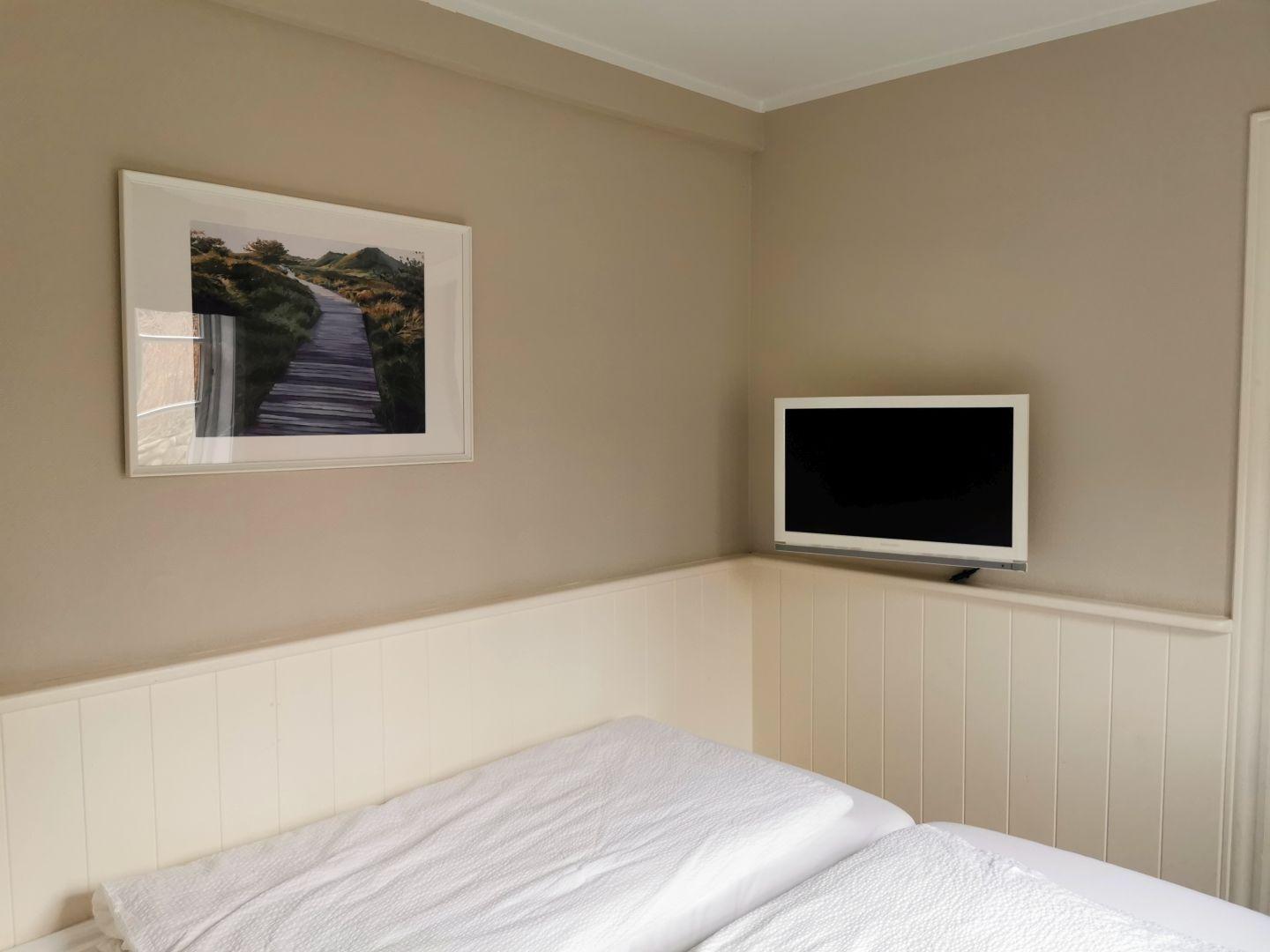 Schlafzimmer mit Bett, Fernseher und Wandbild.