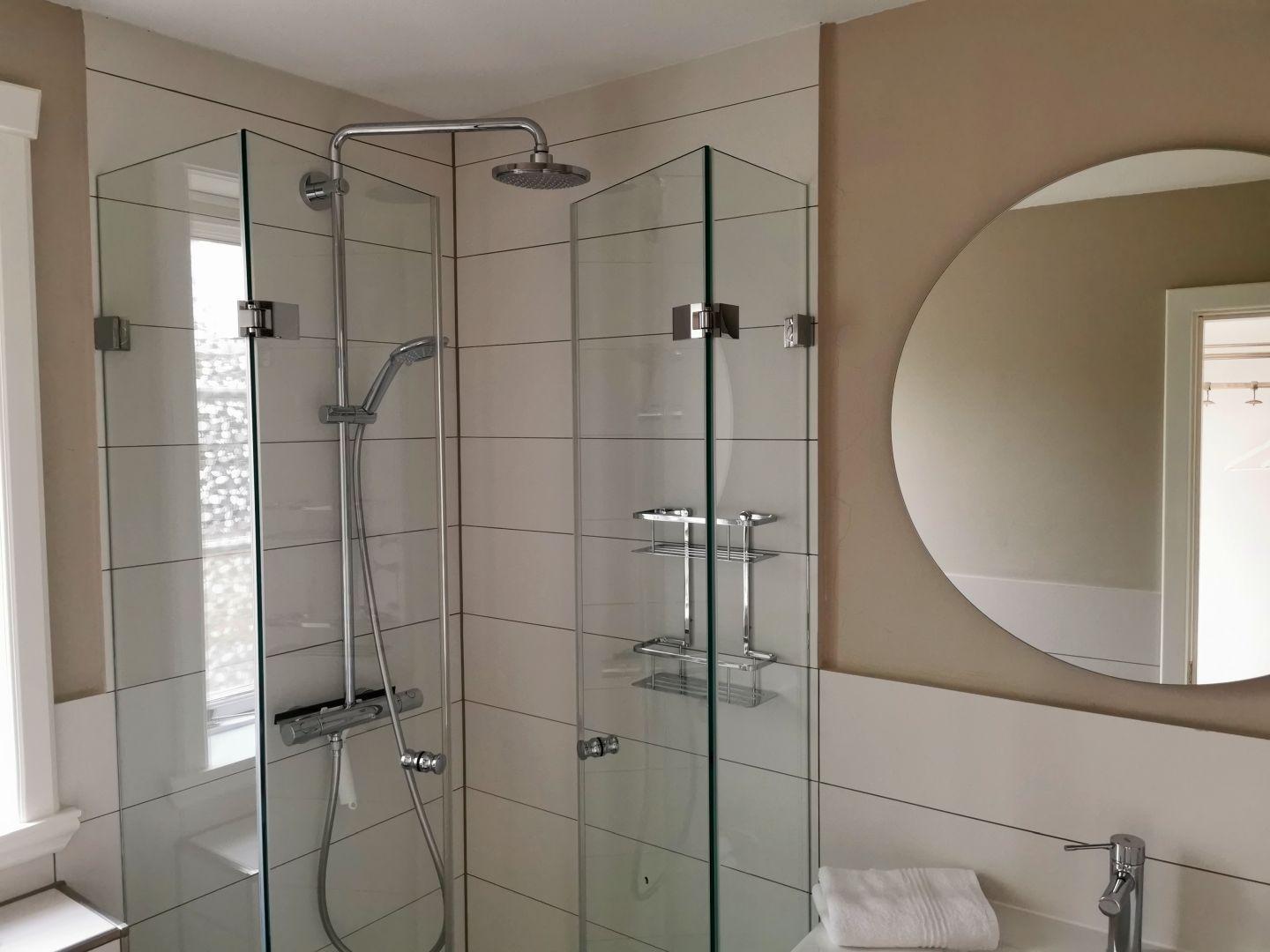 Dusche mit Glaswand, runder Spiegel und Handtuch auf Waschtisch.