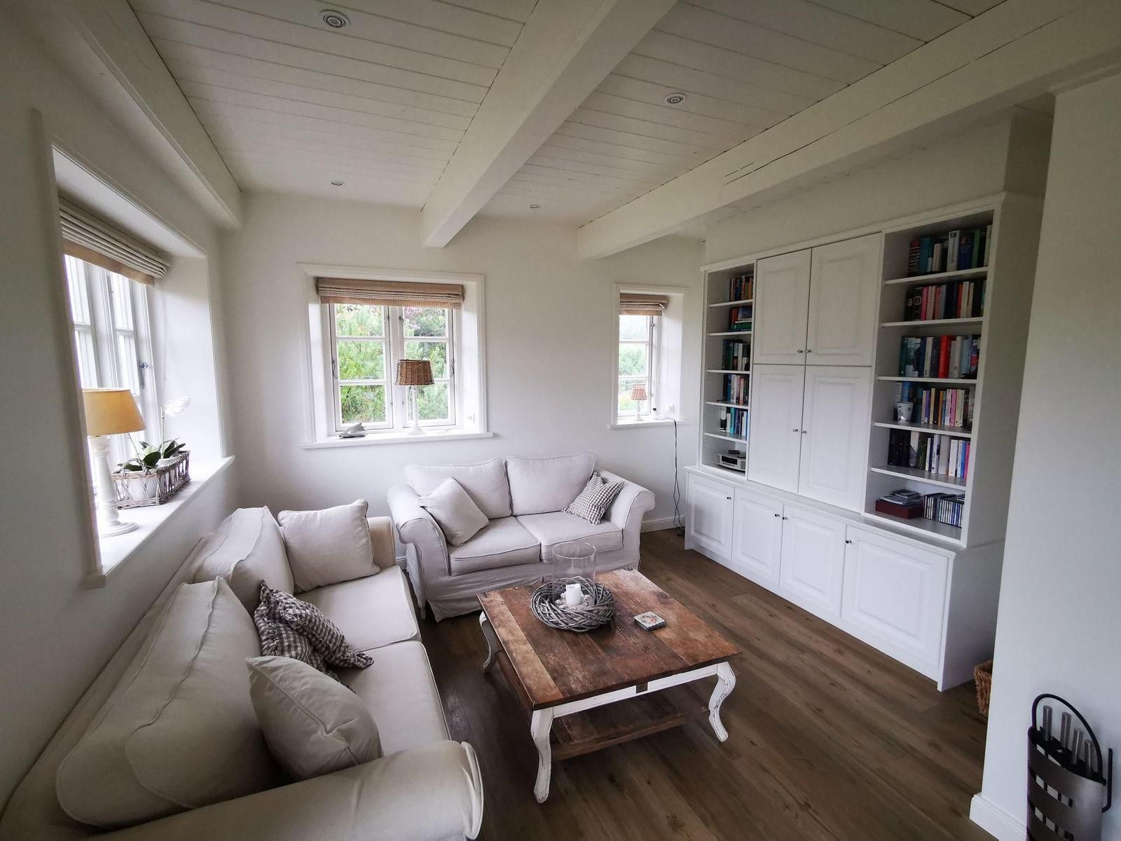 Wohnzimmer mit weißen Sofas, Holztisch und Bücherregal an der Wand.