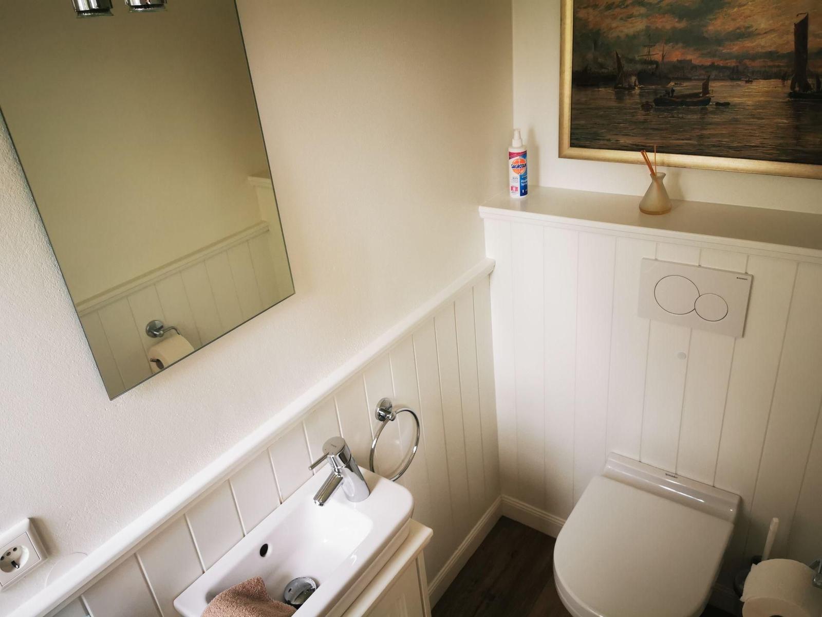 Badezimmer mit Waschbecken, Spiegel, Toilette und Wandbild.