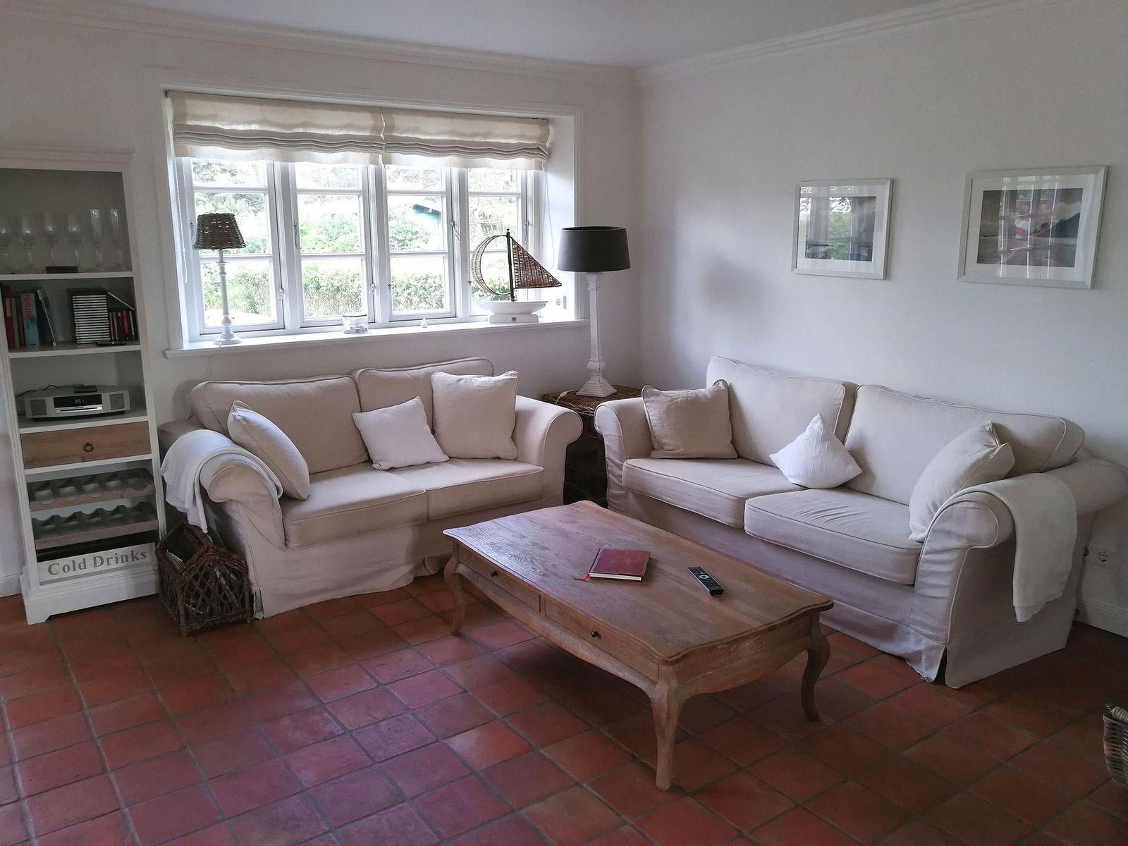 Wohnzimmer mit zwei Sofas, Holztisch und Fenster. Terrakottaboden und weiße Wände.