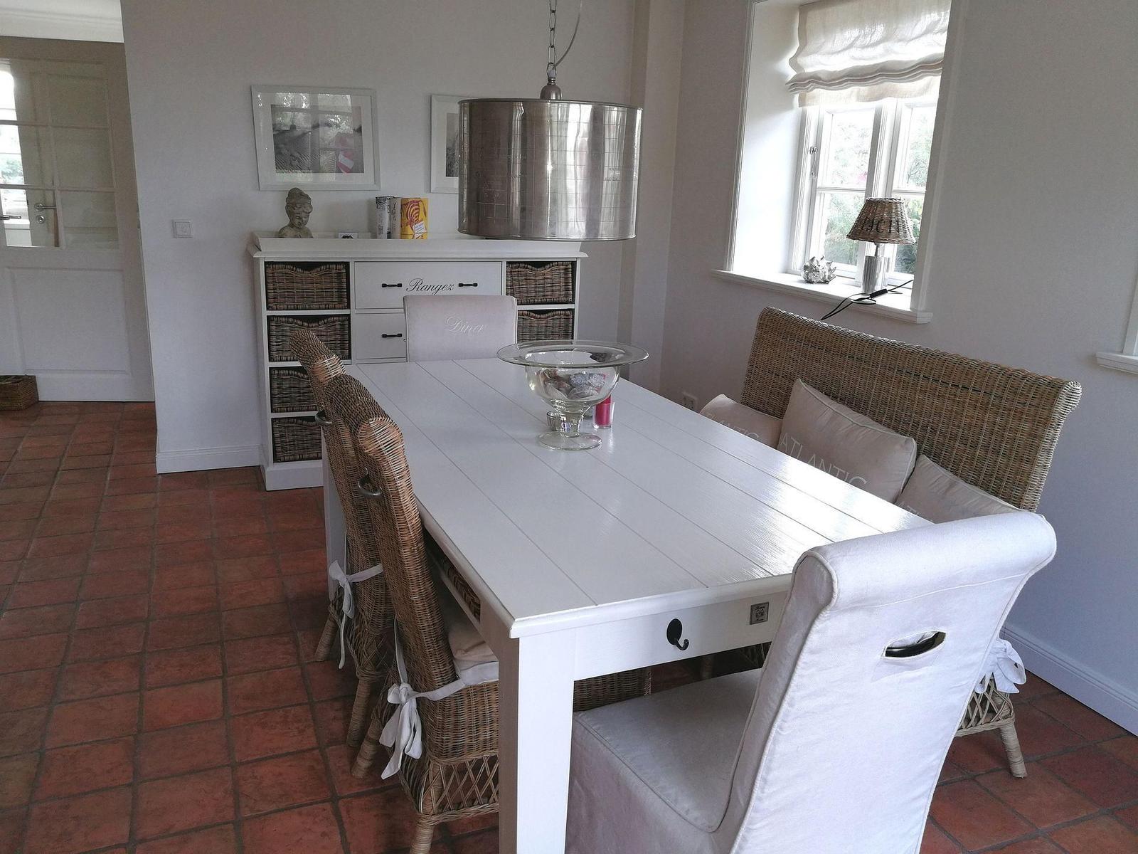 Esszimmer mit weißem Tisch, Rattanstühlen und Fenster