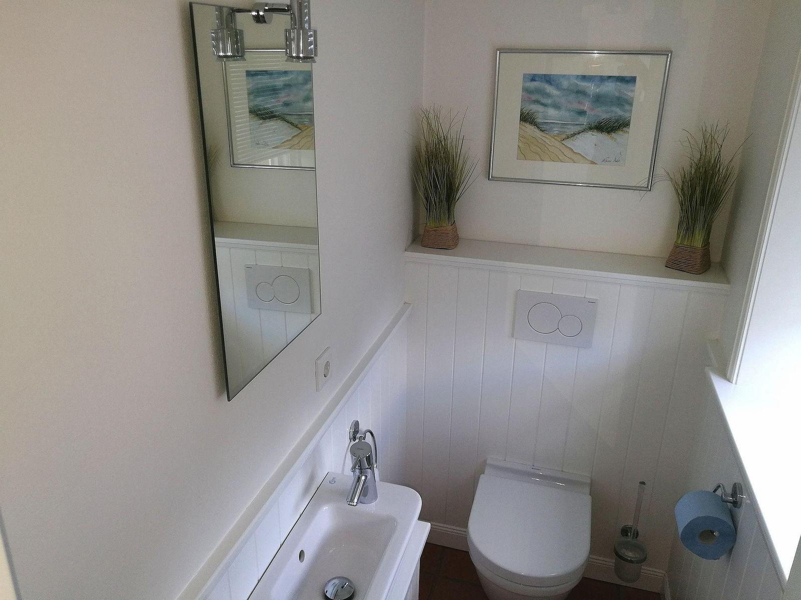 Badezimmer mit Toilette, Waschbecken und Spiegel an der Wand.