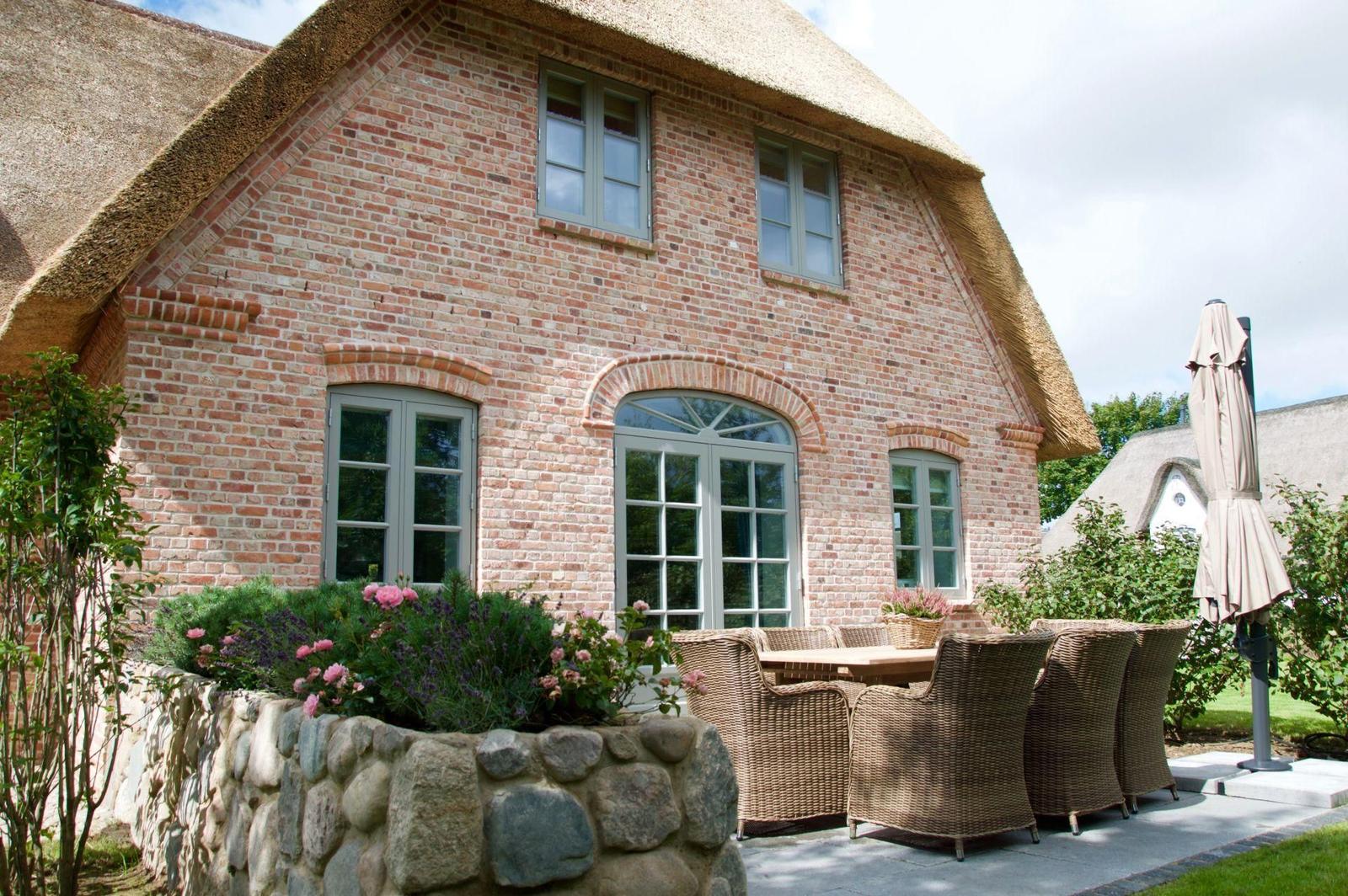 Haus mit Strohdach, Steinmauer, Sitzgruppe und Gartentisch.